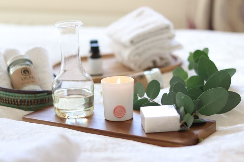 Essential oil bottle, carafe, candle and fresh eucalyptus sprigs on a wooden spa tray with white towels