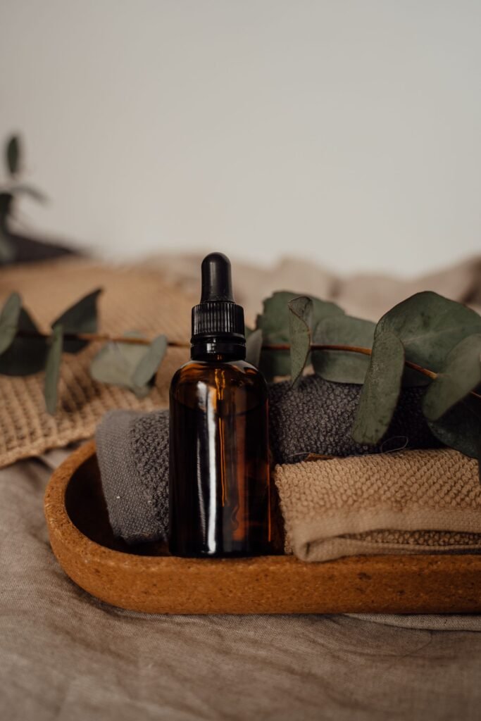 Amber dropper bottle of eucalyptus oil on a wooden tray with folded towels and eucalyptus leaves