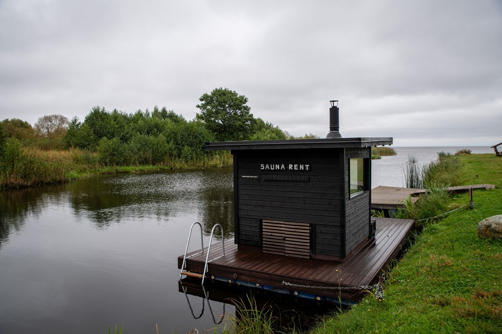Small black wooden sauna on a floating deck beside a quiet lake