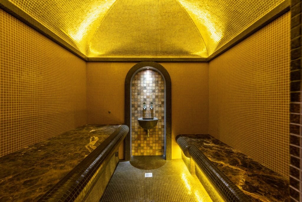 Warmly lit steam room with gold mosaic tiles, a domed ceiling and marble benches on both sides