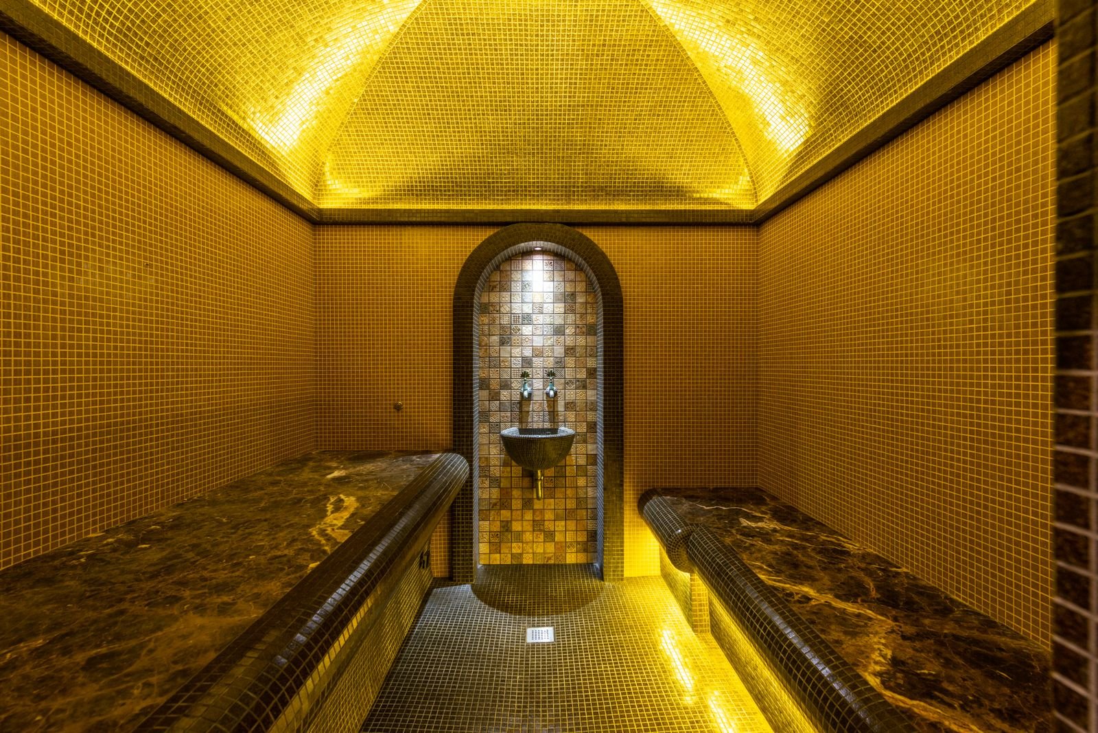Gold mosaic steam room with a vaulted ceiling and marble benches