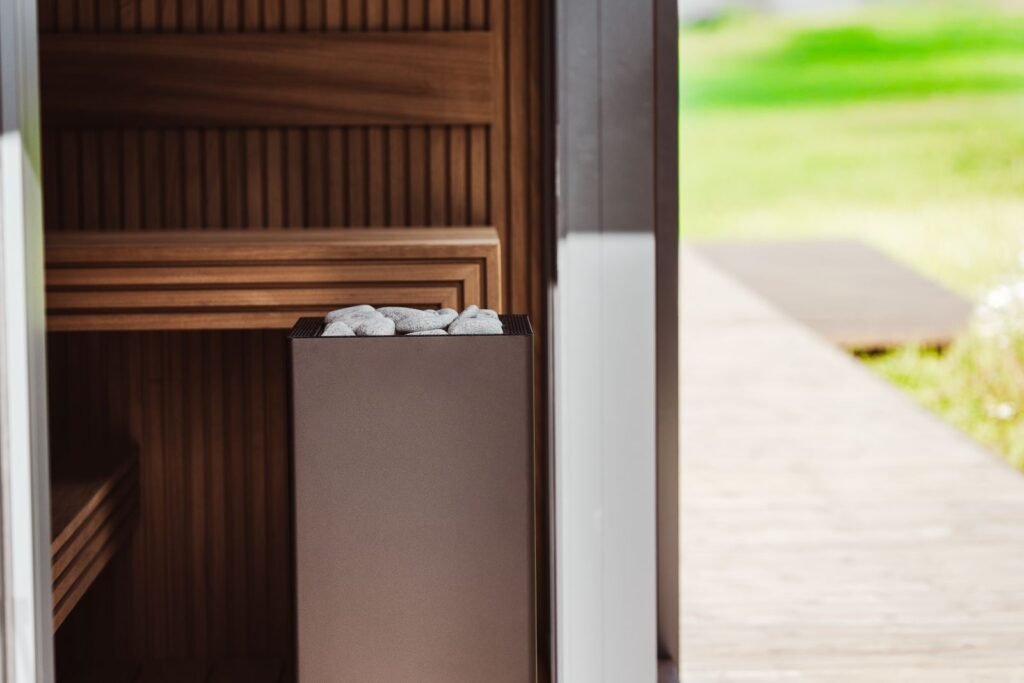Outdoor sauna with the door open, showing wooden benches and an electric heater next to a garden path